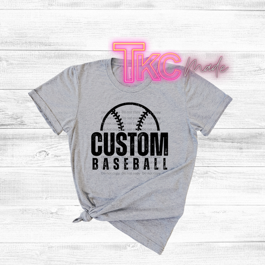 Gray t-shirt with 'Custom Baseball' design on a wooden surface, featuring the brand 'TKC made'.