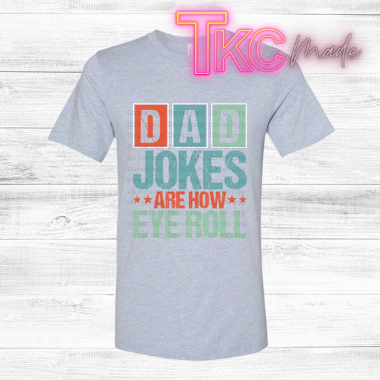 Gray t-shirt with colorful text 'Dad jokes are how eye roll' on a wooden background with 'TKC Made' branding.
