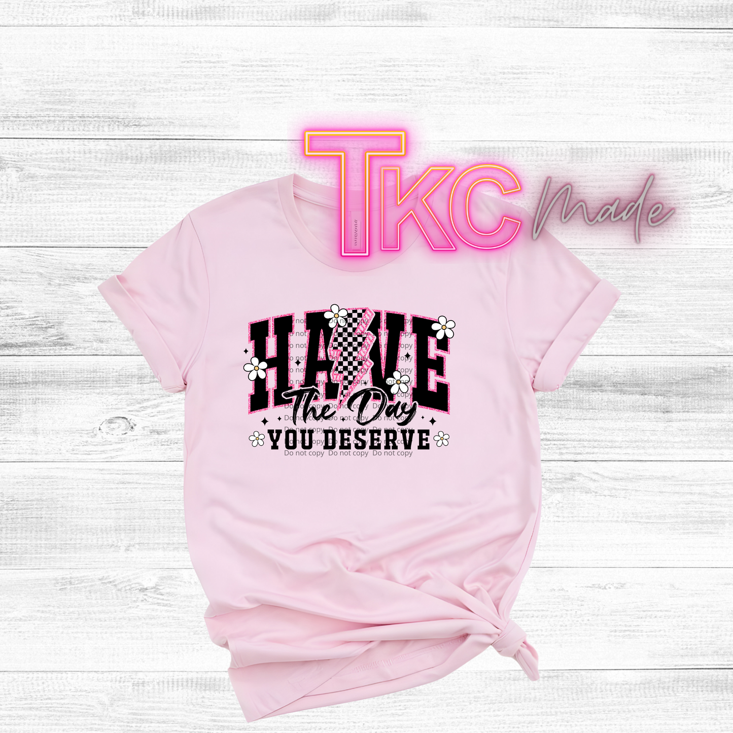 Pink t-shirt with graphic design have the day you deserve and text on a light wooden background