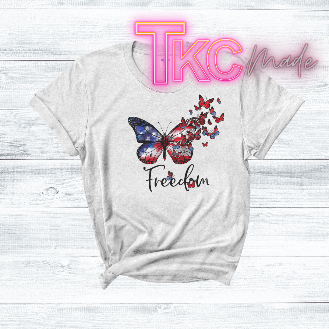 White t-shirt with butterfly design and 'Freedom' text on a white wooden background, featuring 'TKC Made' branding.