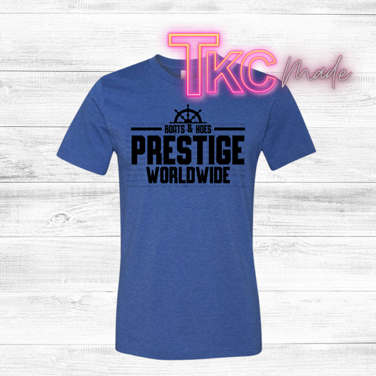 Blue t-shirt with 'PRESTIGE WORLDWIDE' text on a wooden surface with 'TKC made' branding.