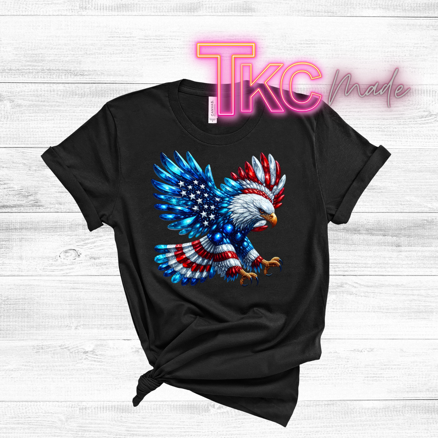 Black t-shirt with a colorful eagle design on a wooden surface, featuring the brand 'TKC Made'.