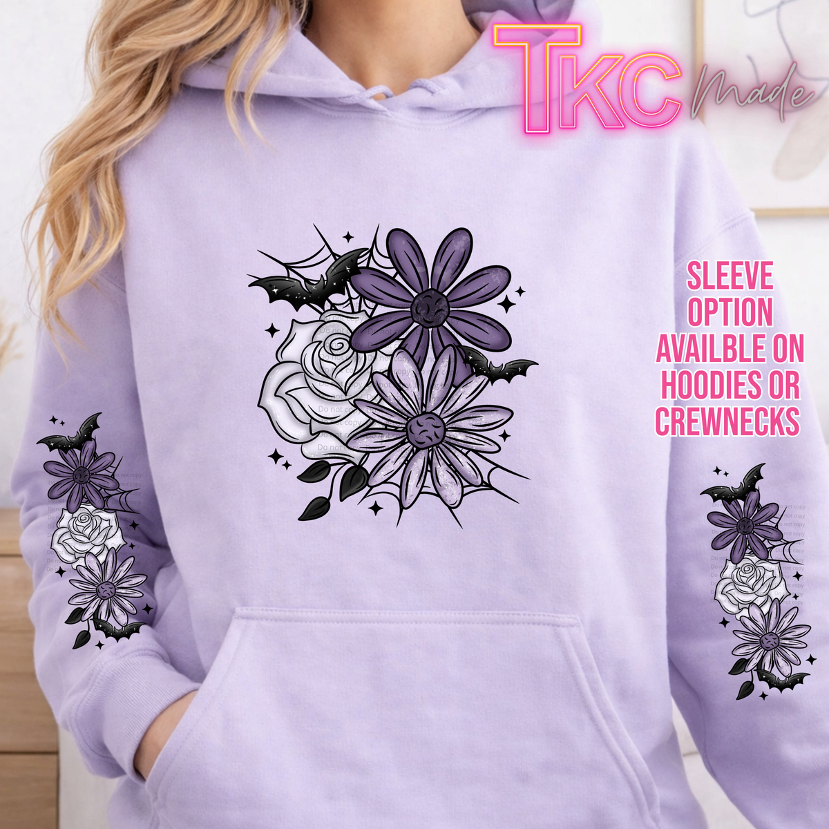 A person wearing a light lavender hoodie with a black and purple floral and bat graphic on the chest and sleeve, plus pink text reading 'Sleeve option available on hoodies or crewnecks' and a 'TKC made' logo.