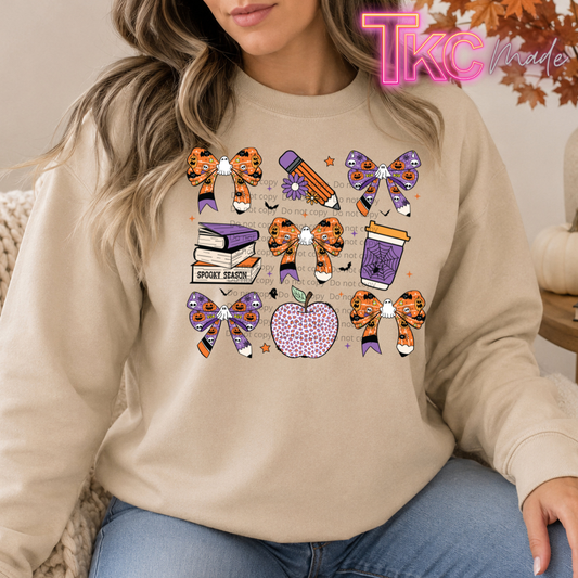 A woman wearing a beige crewneck sweatshirt with a colorful graphic of school sports items like bows, a pencil, books, a coffee cup, an apple, and a banner that reads 'SPOON SEASON'.