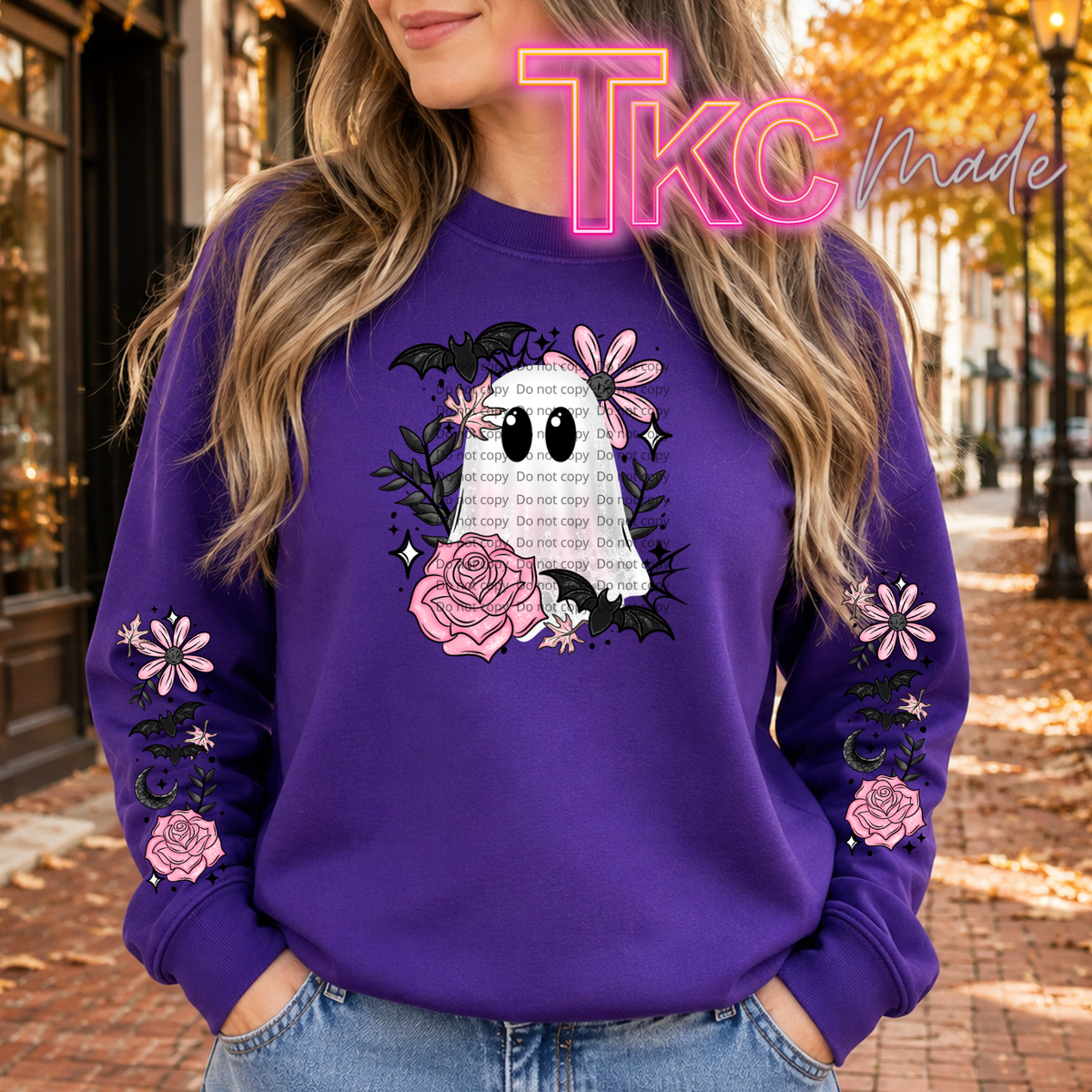 A woman wearing a purple crewneck sweatshirt with a Halloween graphic featuring a ghost, roses, and flowers, with 'do not copy' text on the front and sleeves. The background is a blurred street scene with autumn leaves.