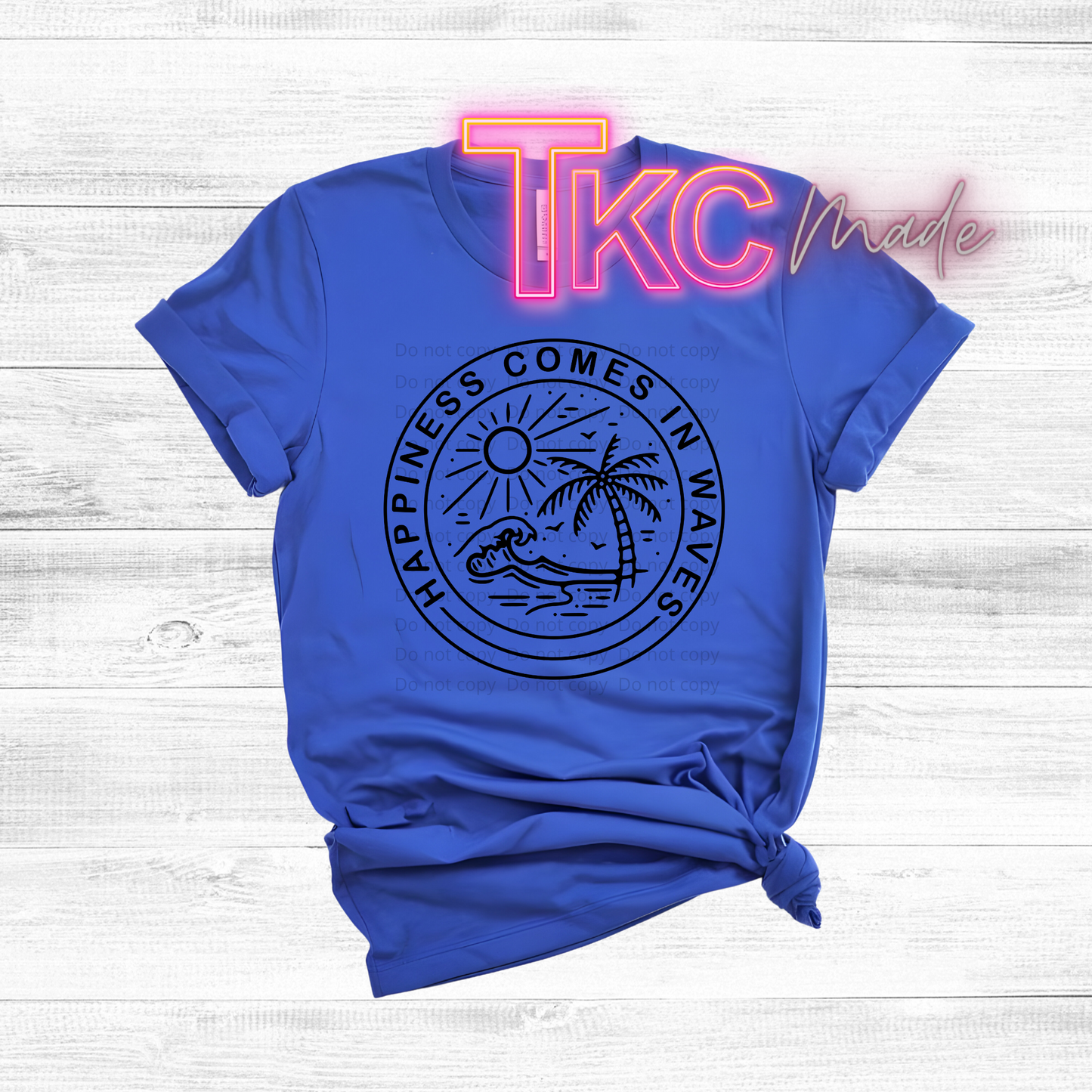 Blue t-shirt with 'Happiness Comes in Waves' design and 'TKC' branding on a light wooden background