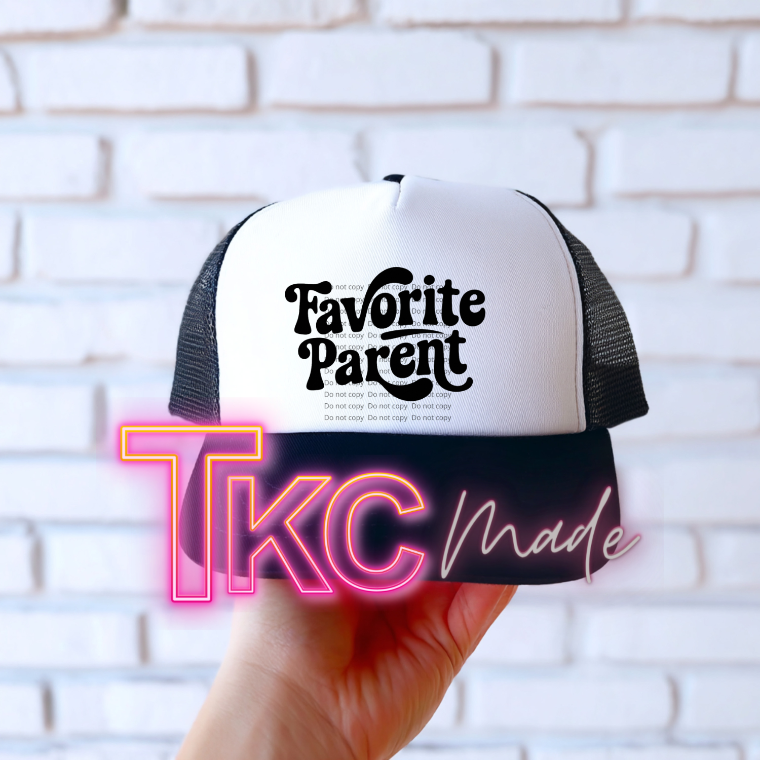 Trucker hat with 'Favorite Parent' text held against a white brick wall.