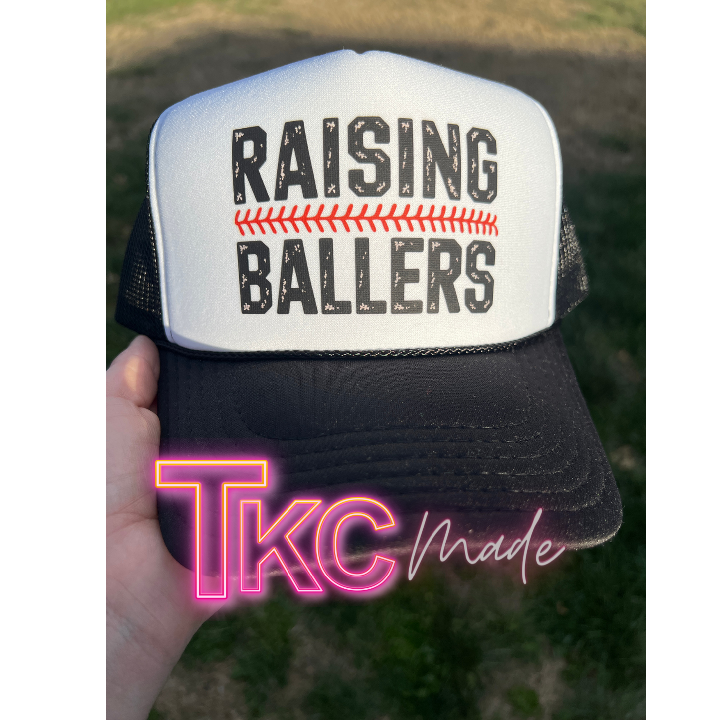 Trucker hat with 'RAISING BALLERS' text held by a hand, with 'TkC Made' branding.