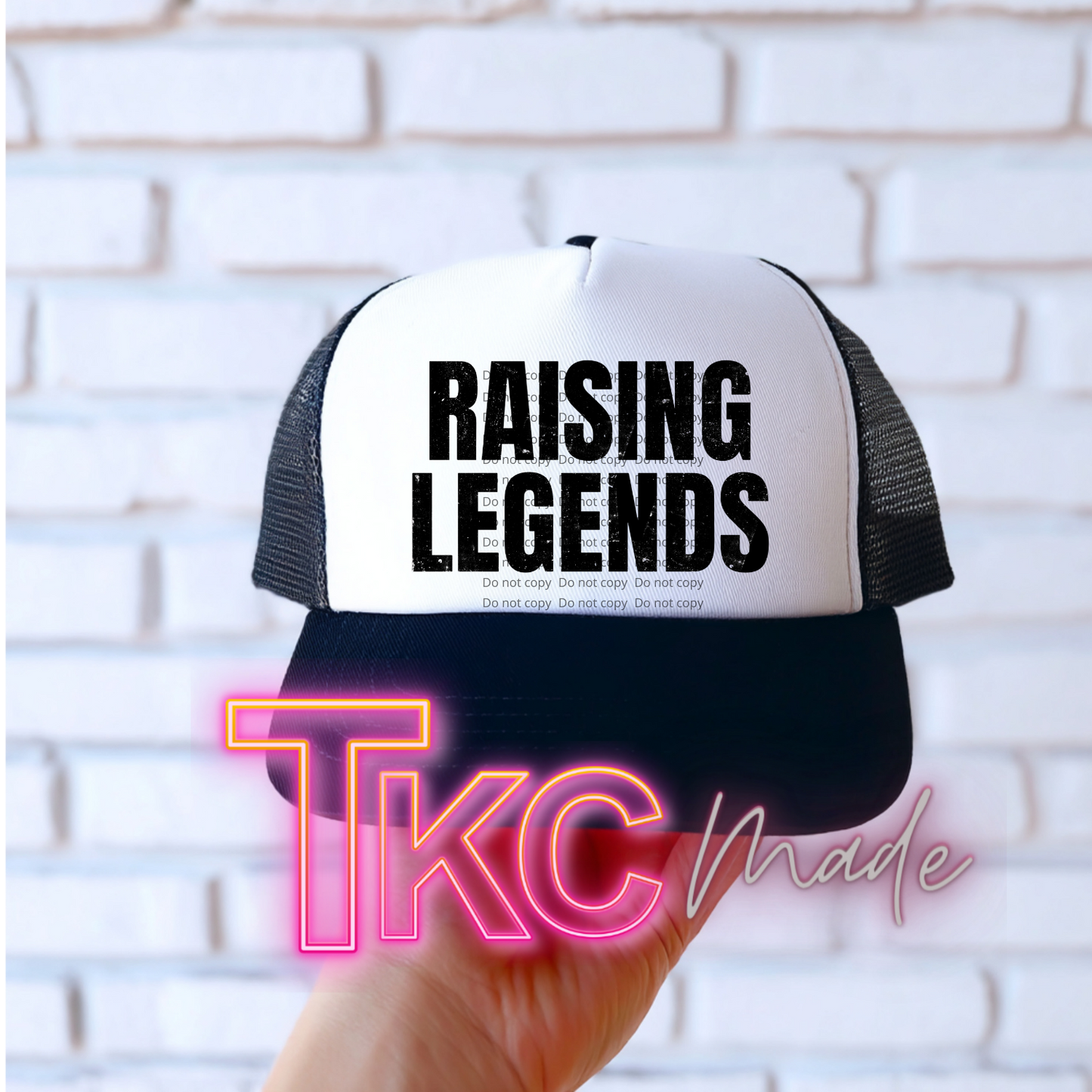 Trucker hat with 'RAISING LEGENDS' text held against a white brick wall, with 'TKC Made' branding.