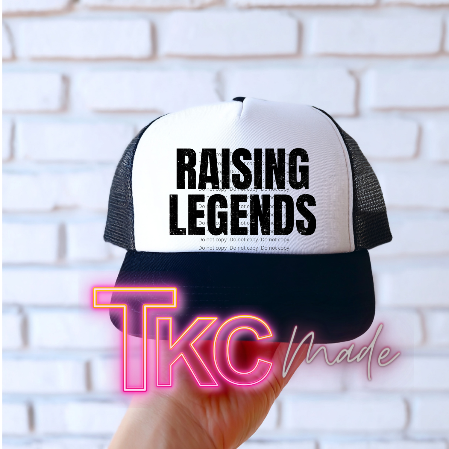 Trucker hat with 'RAISING LEGENDS' text held against a white brick wall, with 'TKC Made' branding.