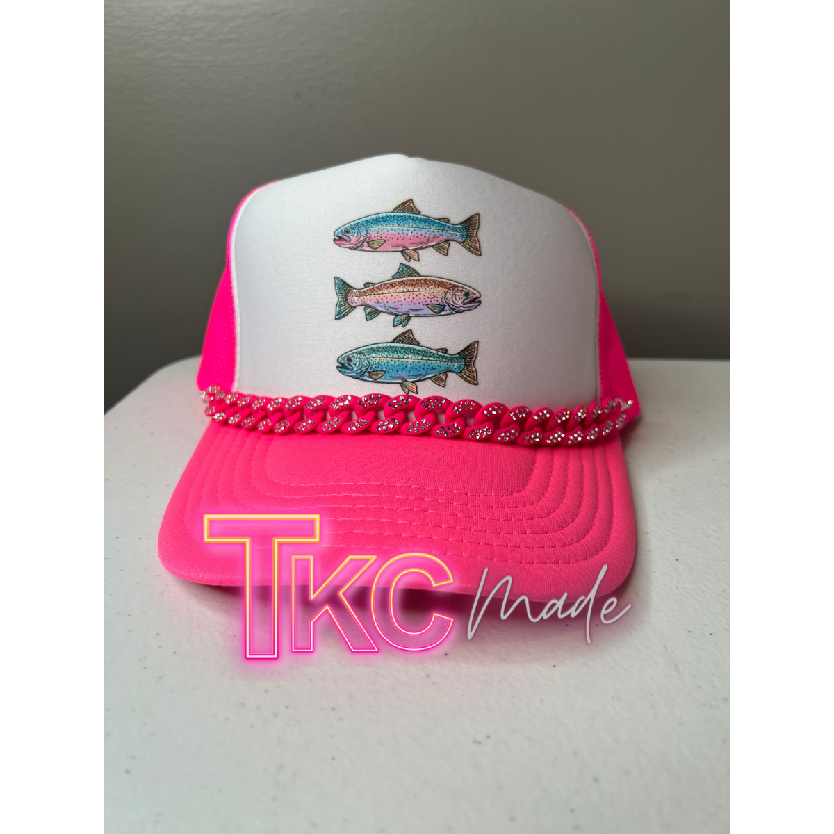 Pink and white cap with fish designs on a white surface, featuring 'TKC Made' branding.
