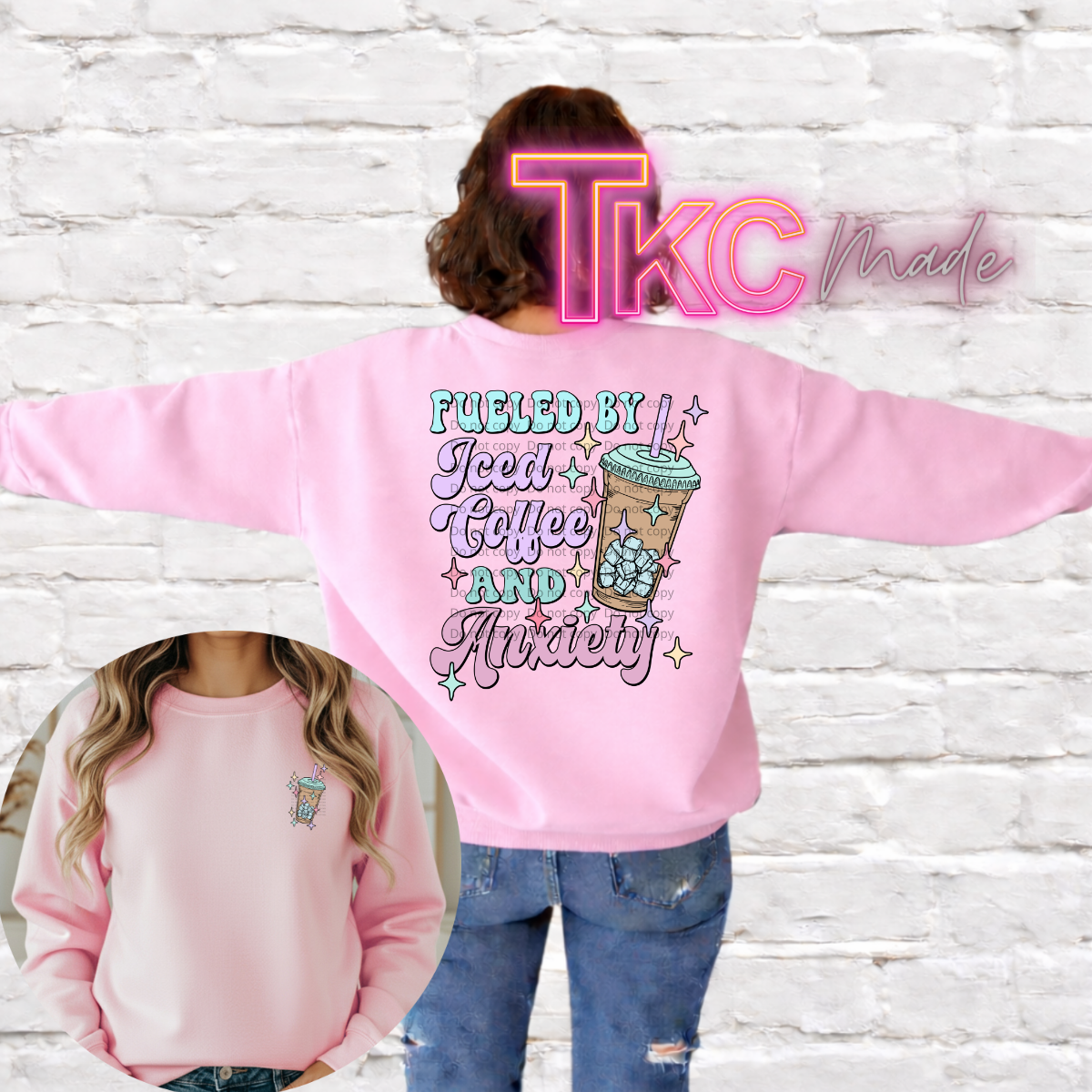 Pink sweatshirt with text fueled by iced coffee and anxiety the back,  and a iced coffee drink on the front pocket area. worn by a person against a white brick wall.