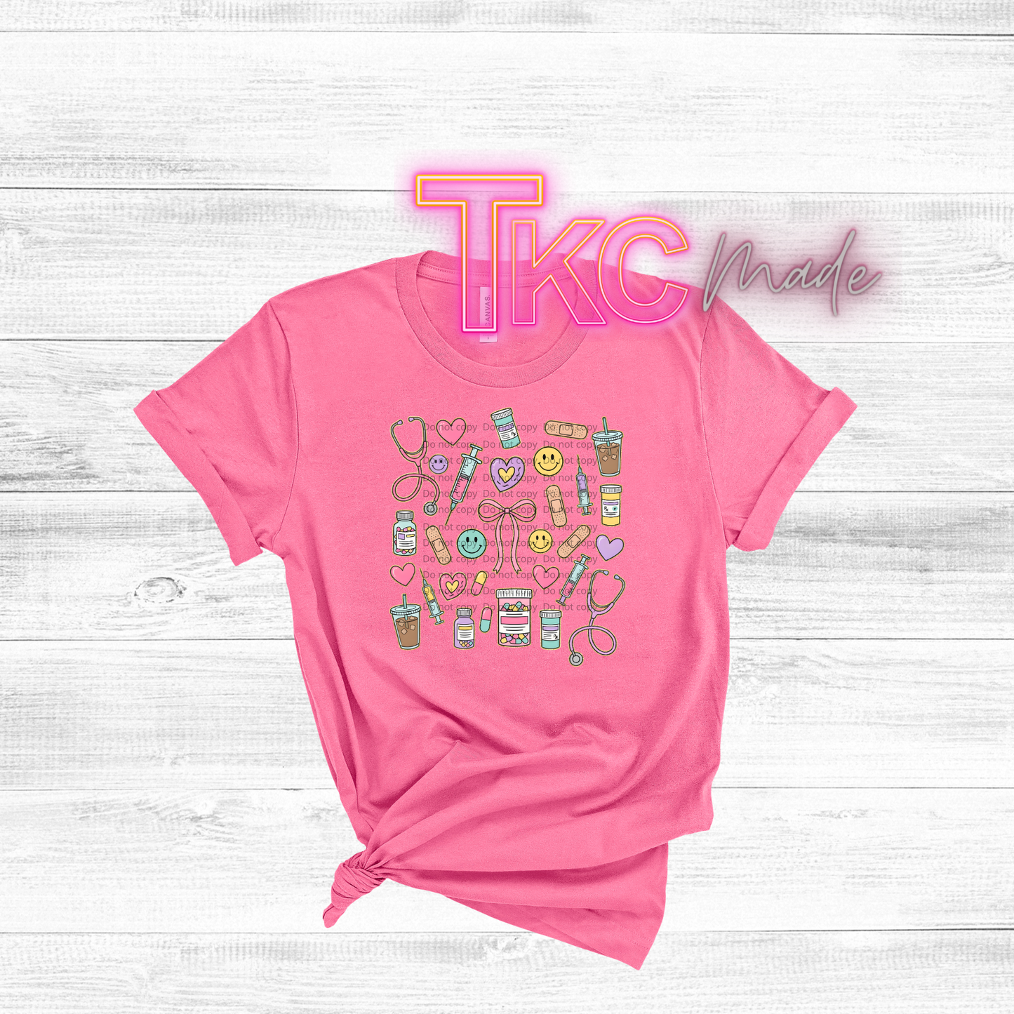 Pink t-shirt with colorful medical nurse graphics and 'TKC Made' text on a white wooden background