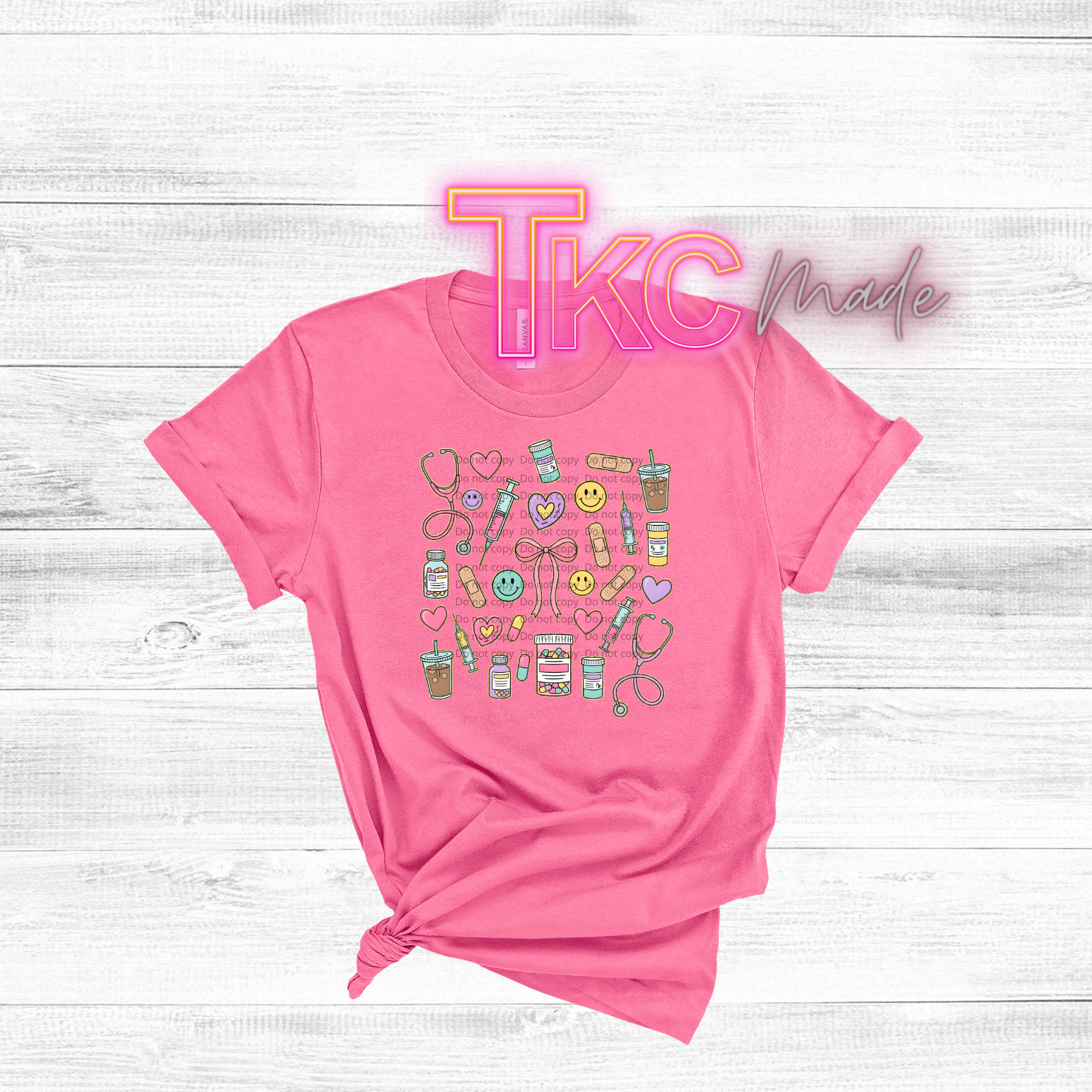 Pink t-shirt with colorful medical nurse graphics and 'TKC Made' text on a white wooden background