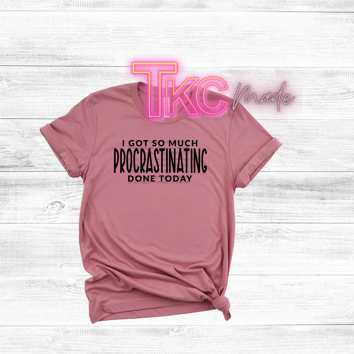 Pink t-shirt with text 'I got so much procrastinating done today' on a light wooden surface.