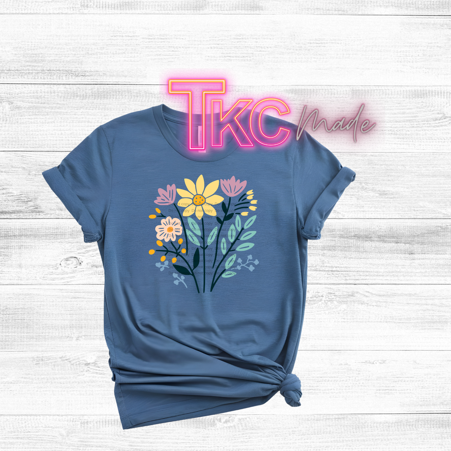 Blue t-shirt with floral design on a white wooden background with 'TKC Made' text.