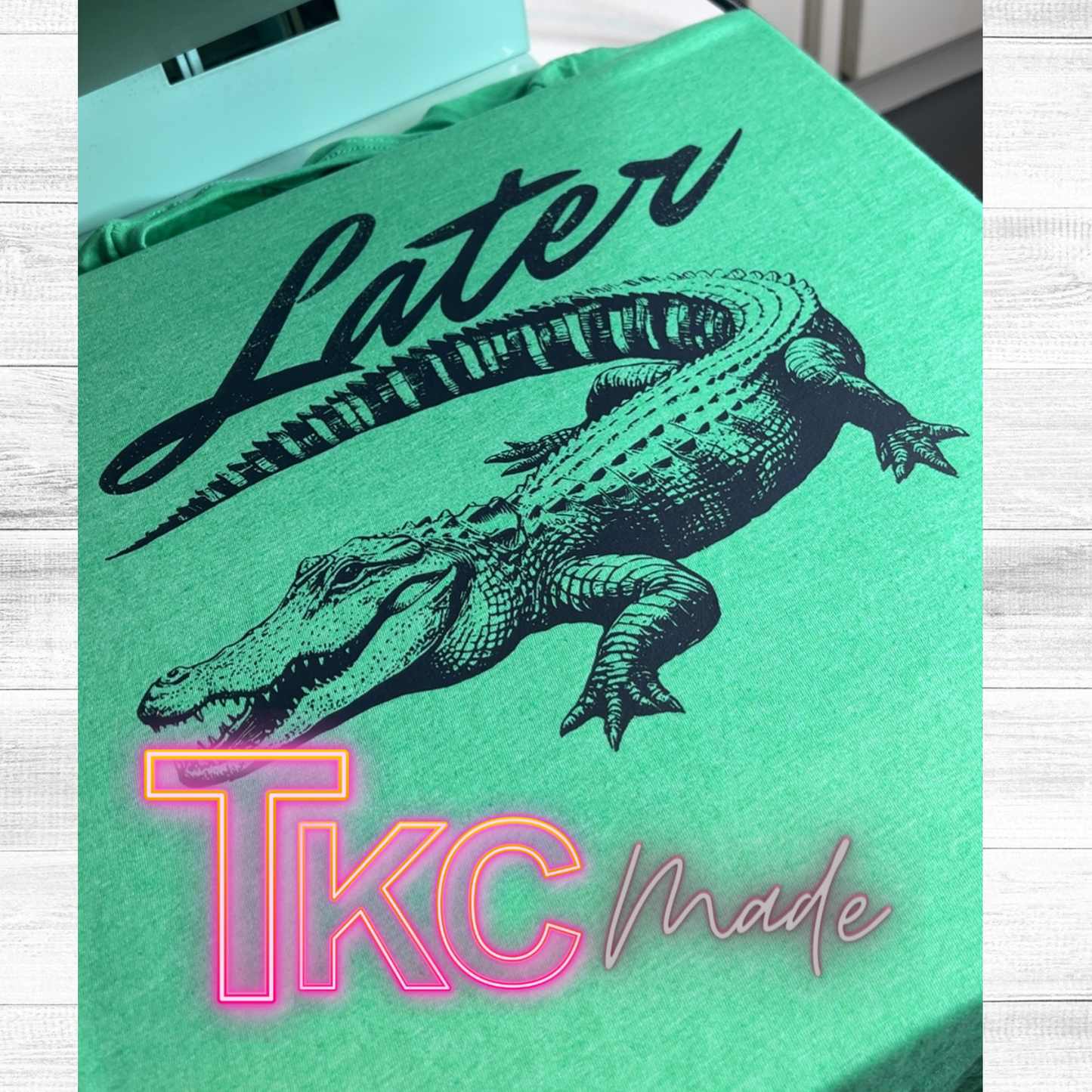 Green t-shirt with an alligator graphic and 'TKC Made' text on a light wooden surface.