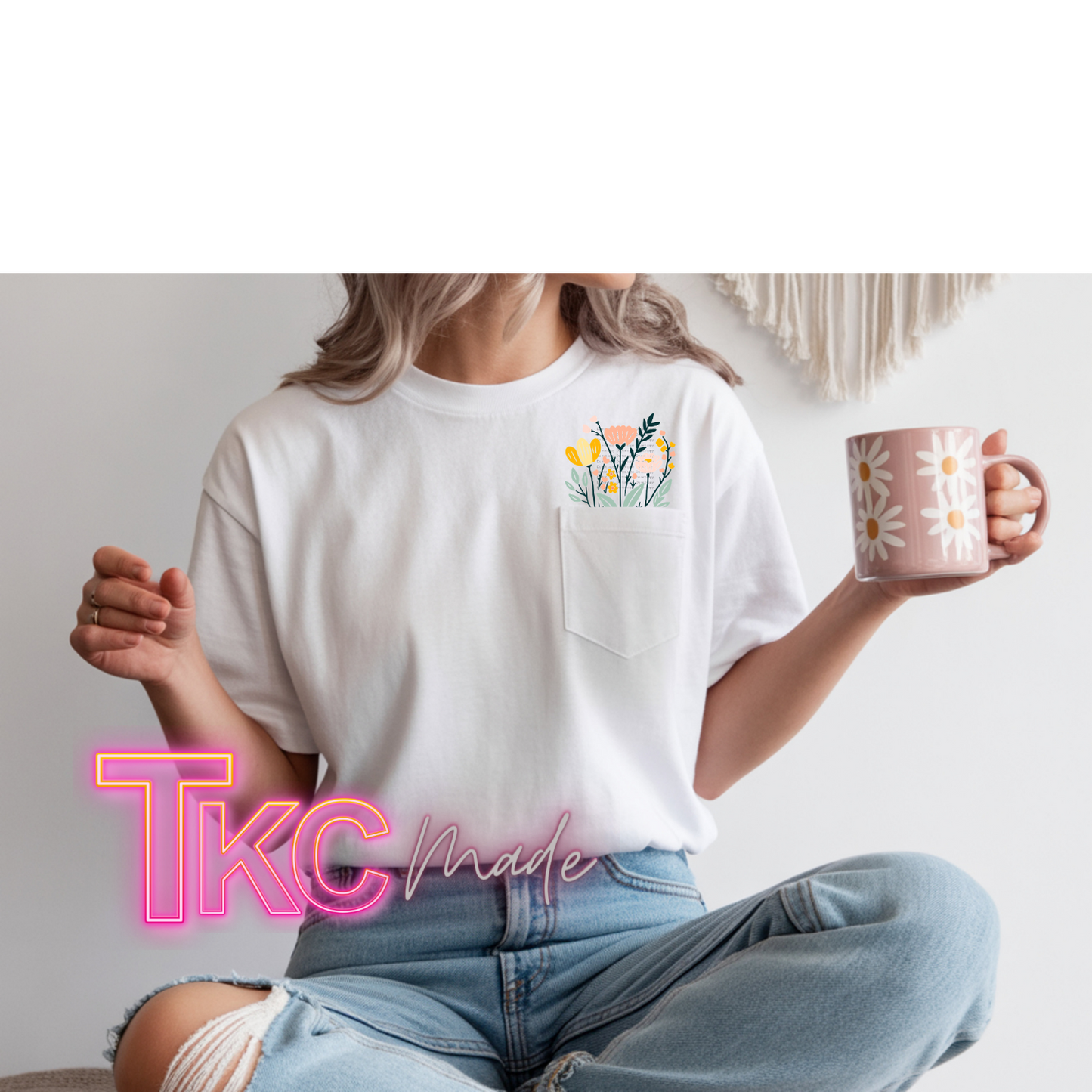 Person wearing a white t-shirt with a floral design and holding a mug, sitting on a couch.
