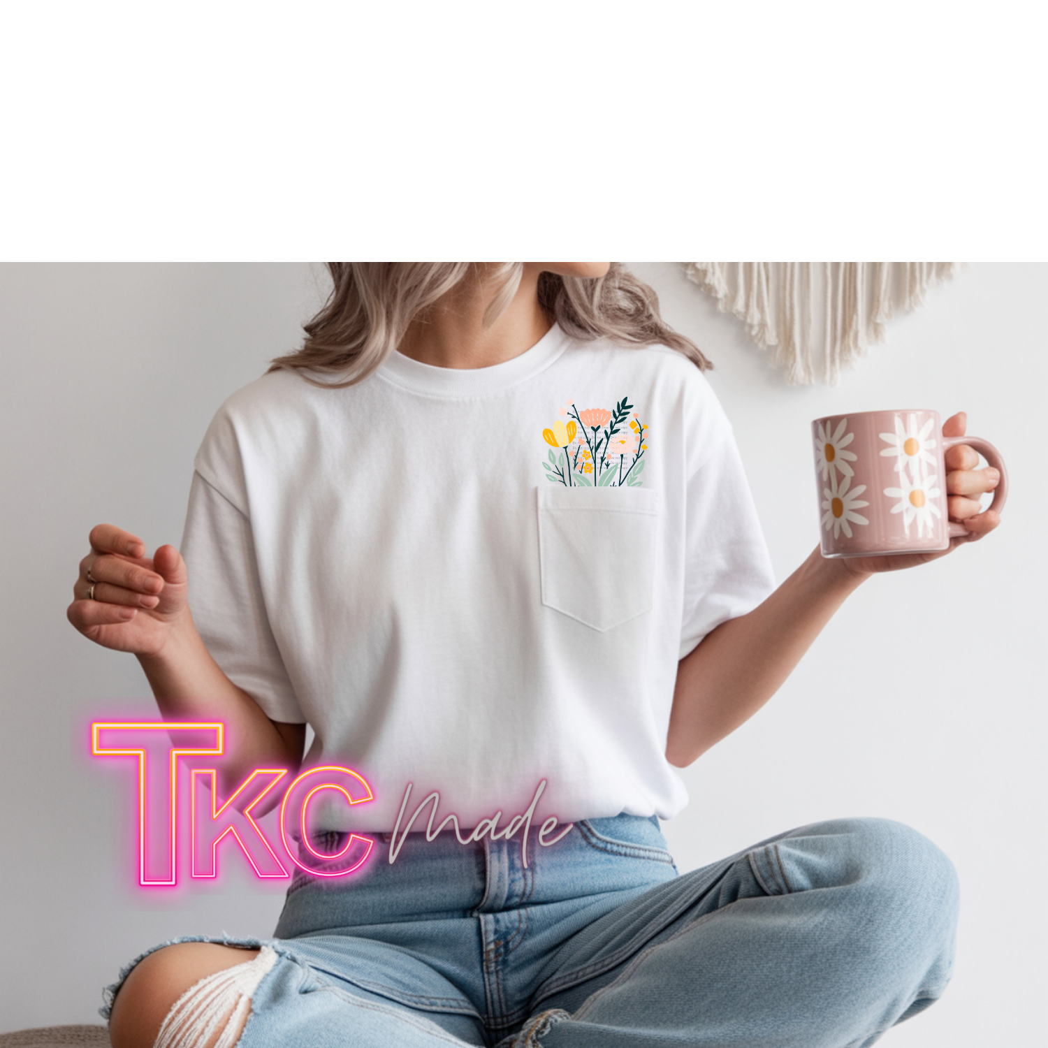 Person wearing a white t-shirt with a floral design and holding a mug, sitting on a couch.