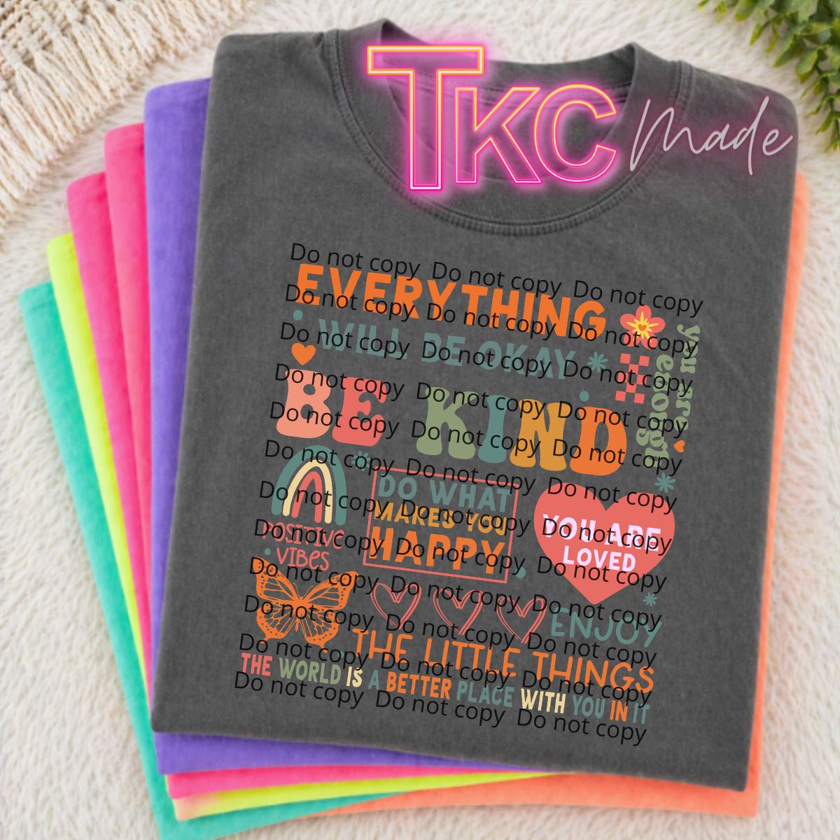 Stack of colorful t-shirts with text and 'TKC Made' branding on a textured surface.