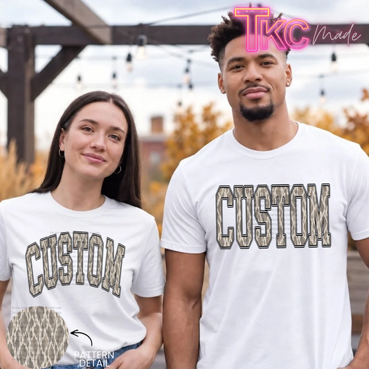 A man and a woman wearing matching white custom-printed t-shirts with a camouflage patterned 'CUSTOM' graphic on the chest, set against an outdoor background with a 'TKC Made' logo overlay.