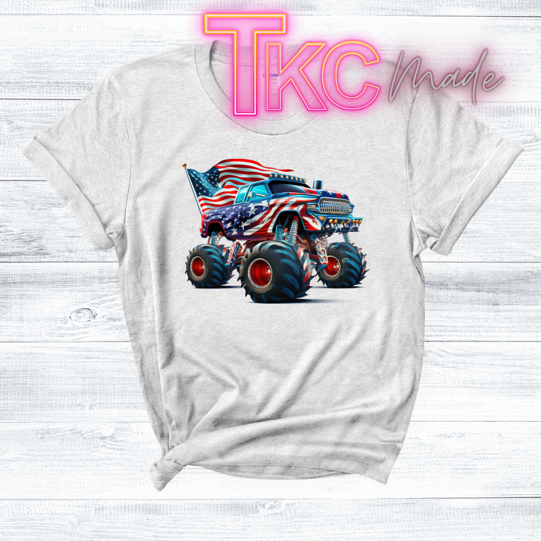 White t-shirt with a graphic of a monster truck with an American flag design, on a light wooden surface with 'TKC made' text.
