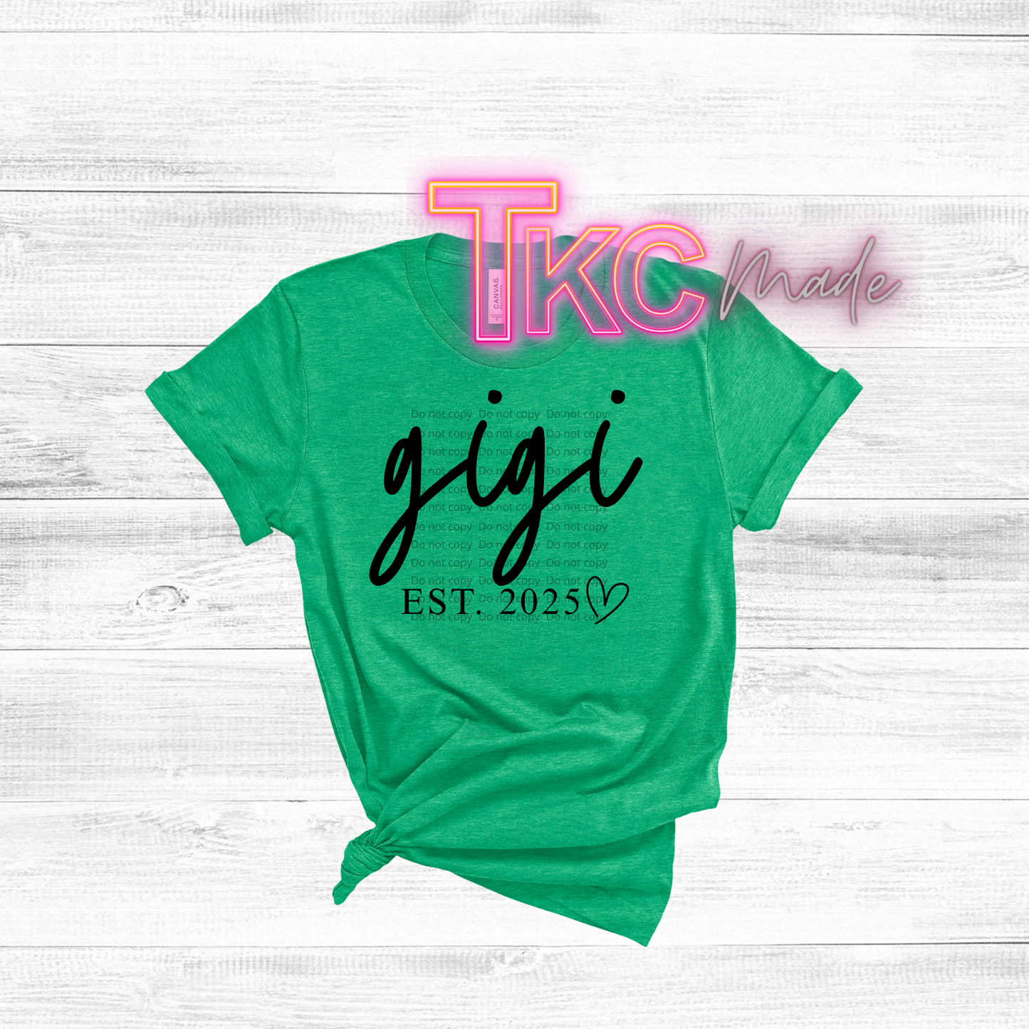 Green t-shirt with 'gigi EST. 2025' text on a white wooden background