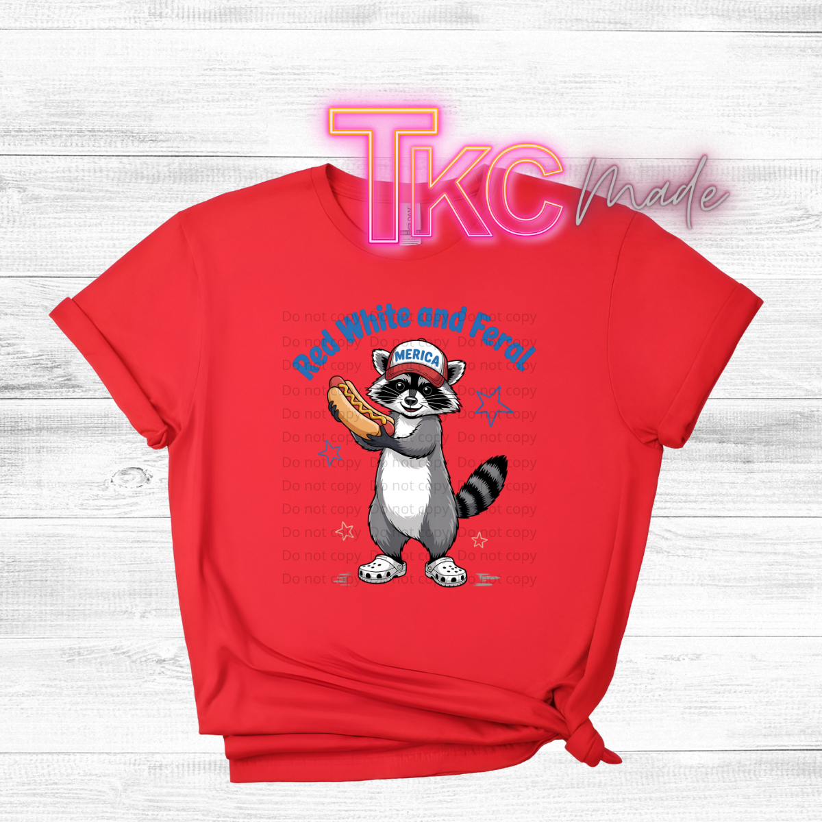 Red t-shirt with a raccoon holding a hot dog graphic and text on a light wooden background.