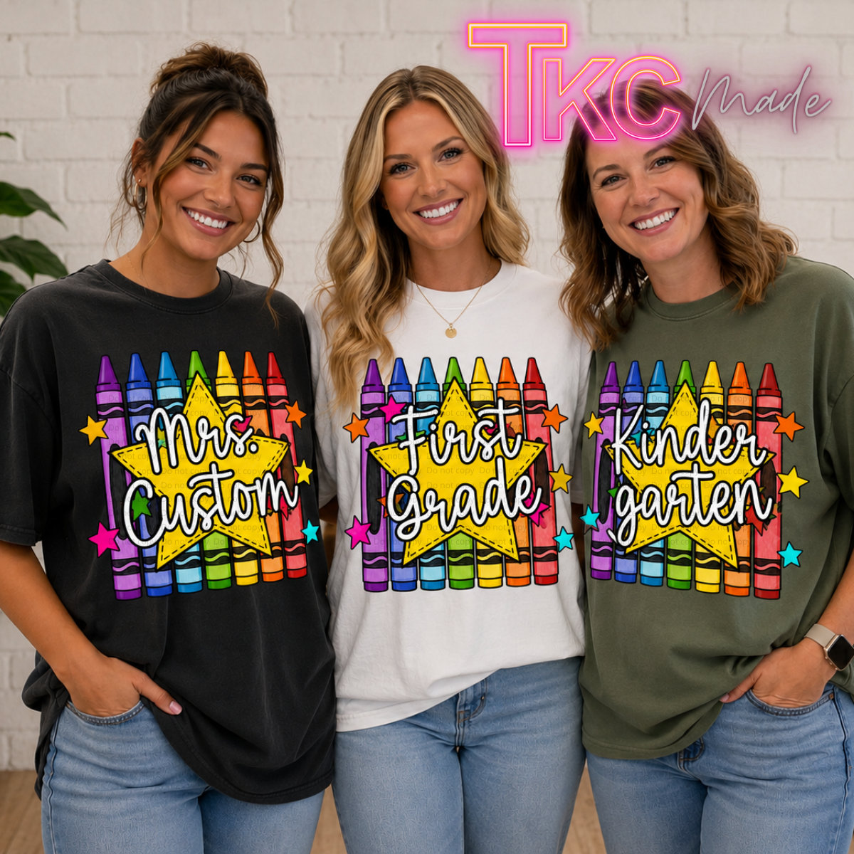 Three women standing side by side wearing graphic t-shirts with crayon designs and text reading 'Mrs. Custom', 'First Grade', and 'Kinder garten'.