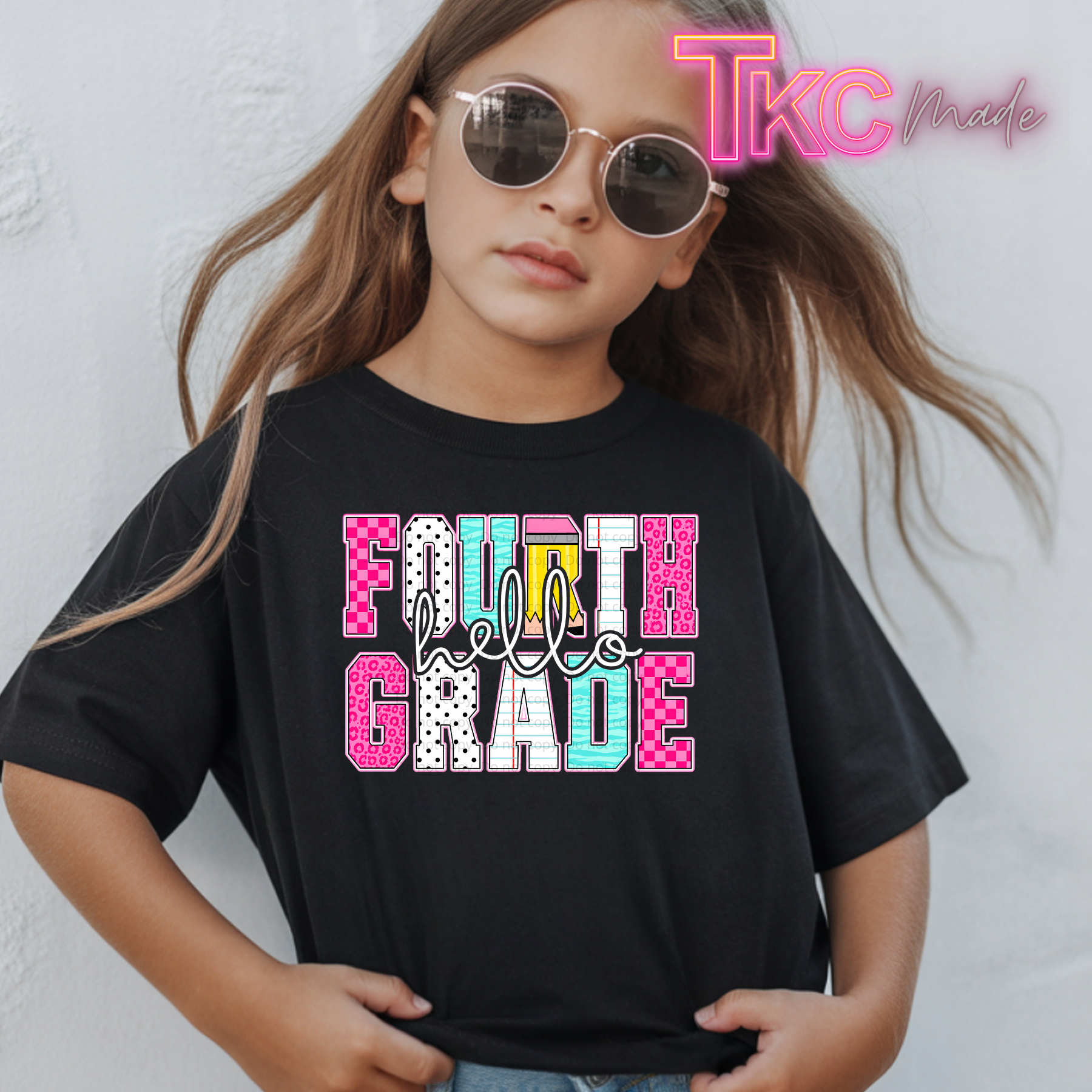 A young girl with long light brown hair wearing round sunglasses and a black graphic t-shirt that reads 'FOURTH Grade' in pink, white, and light blue patterned letters. A 'TKC Made' watermark is visible in the top right corner.