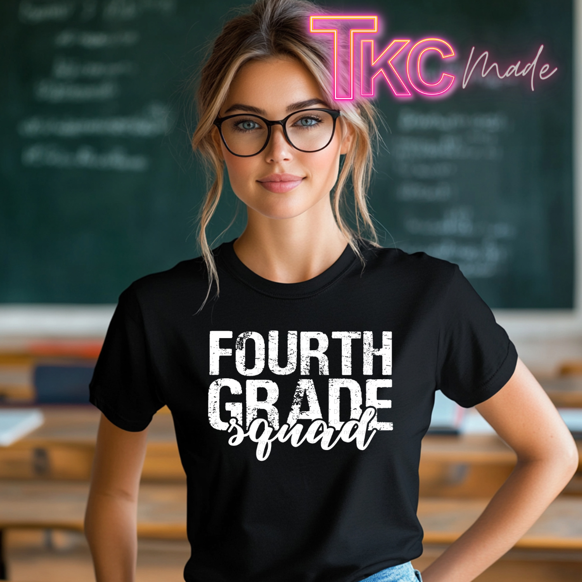 A woman wearing a black graphic t-shirt with the text 'FOURTH GRADE squad' in white, standing in a blurred classroom setting with a chalkboard behind her. A pink and yellow 'TKC made' logo watermark is visible in the top right corner.