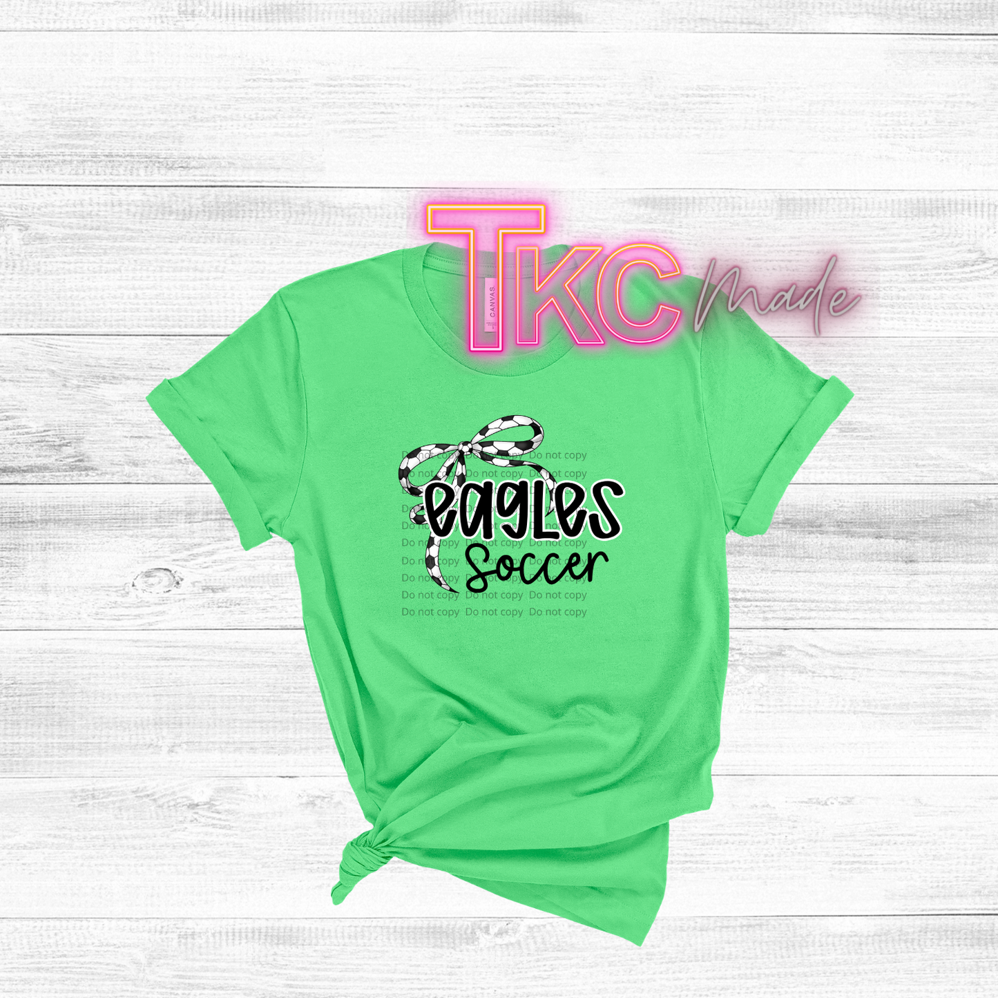 Green t-shirt with 'Eagles Soccer' design on a white wooden background, featuring the brand 'TKC Made'.