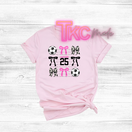Pink t-shirt with soccer graphics and text on a white wooden background