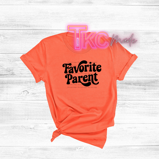 Orange t-shirt with 'Favorite Parent' text on a white wooden background