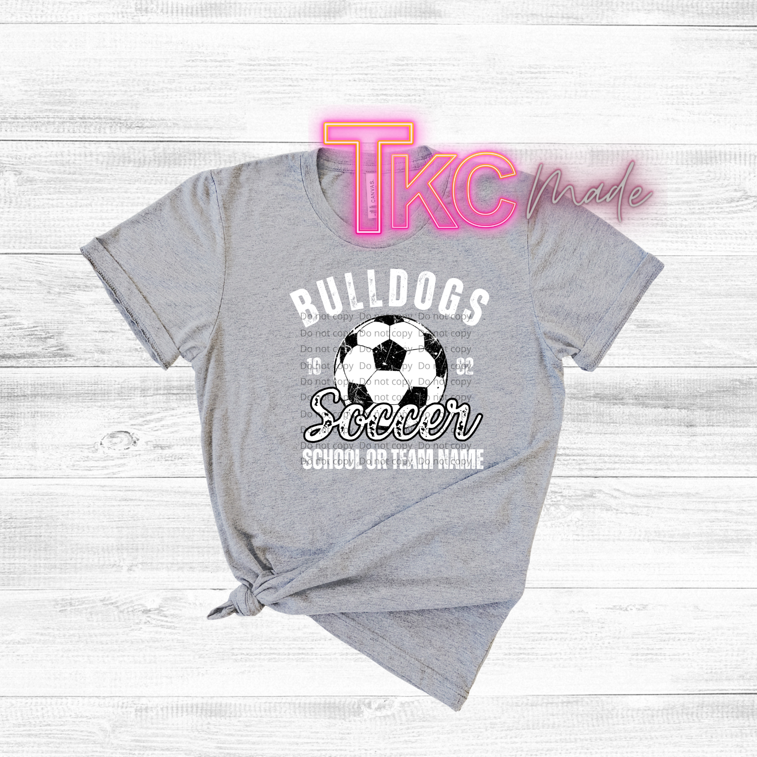 Gray t-shirt with soccer design and 'TKC made' text on a light wooden background