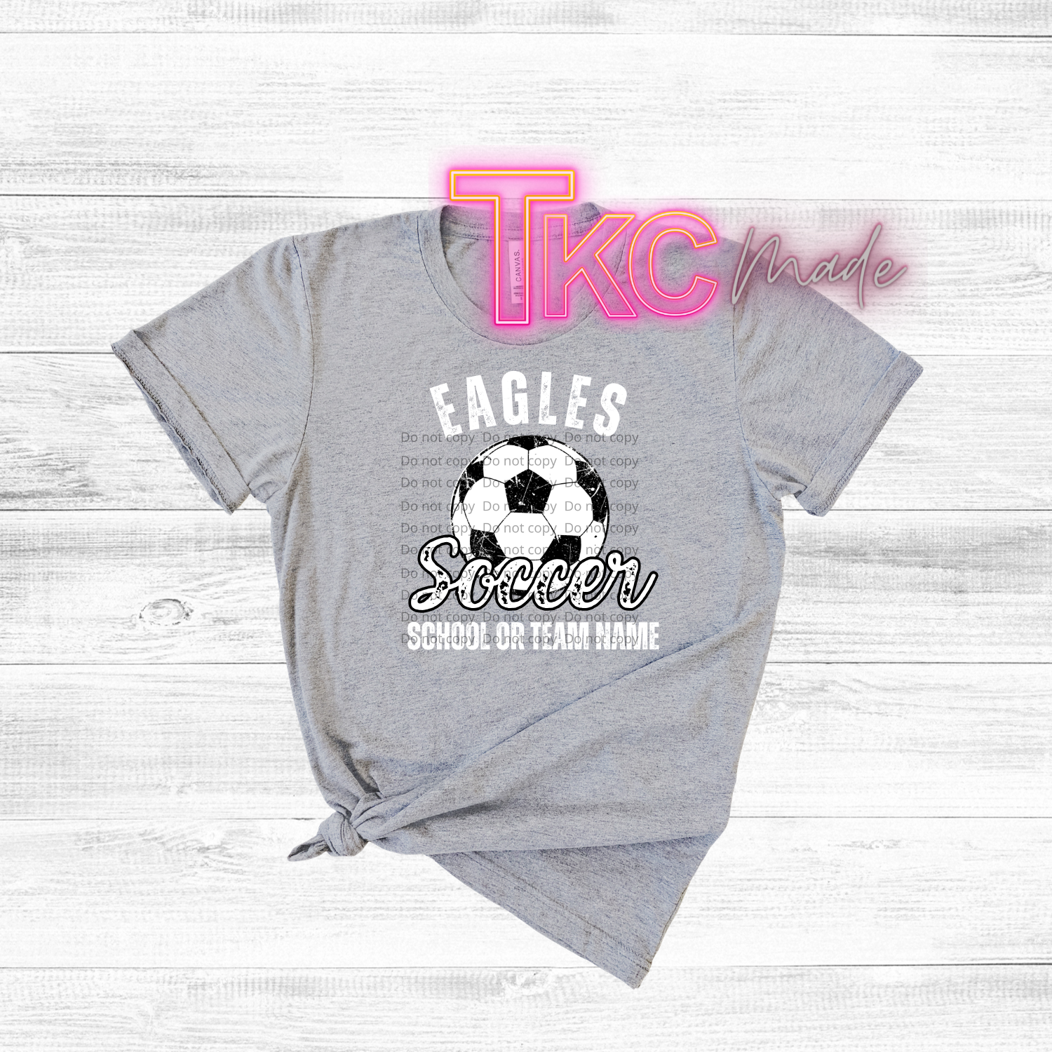 Gray t-shirt with soccer design and text on a wooden surface, featuring 'TKC made' branding.
