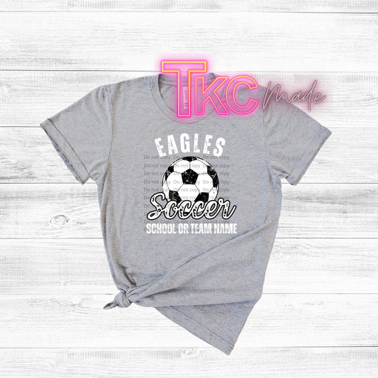 Gray t-shirt with soccer design and text on a wooden surface, featuring 'TKC made' branding.