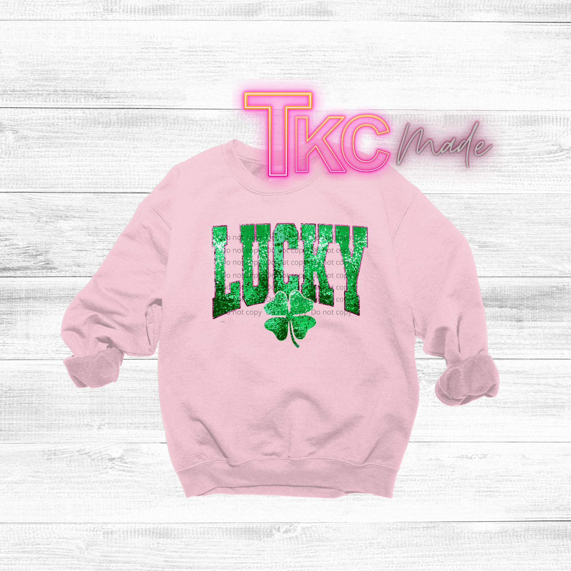 Pink sweatshirt with 'LUCKY' and clover graphic on a white wooden background, featuring 'TKC made' text.