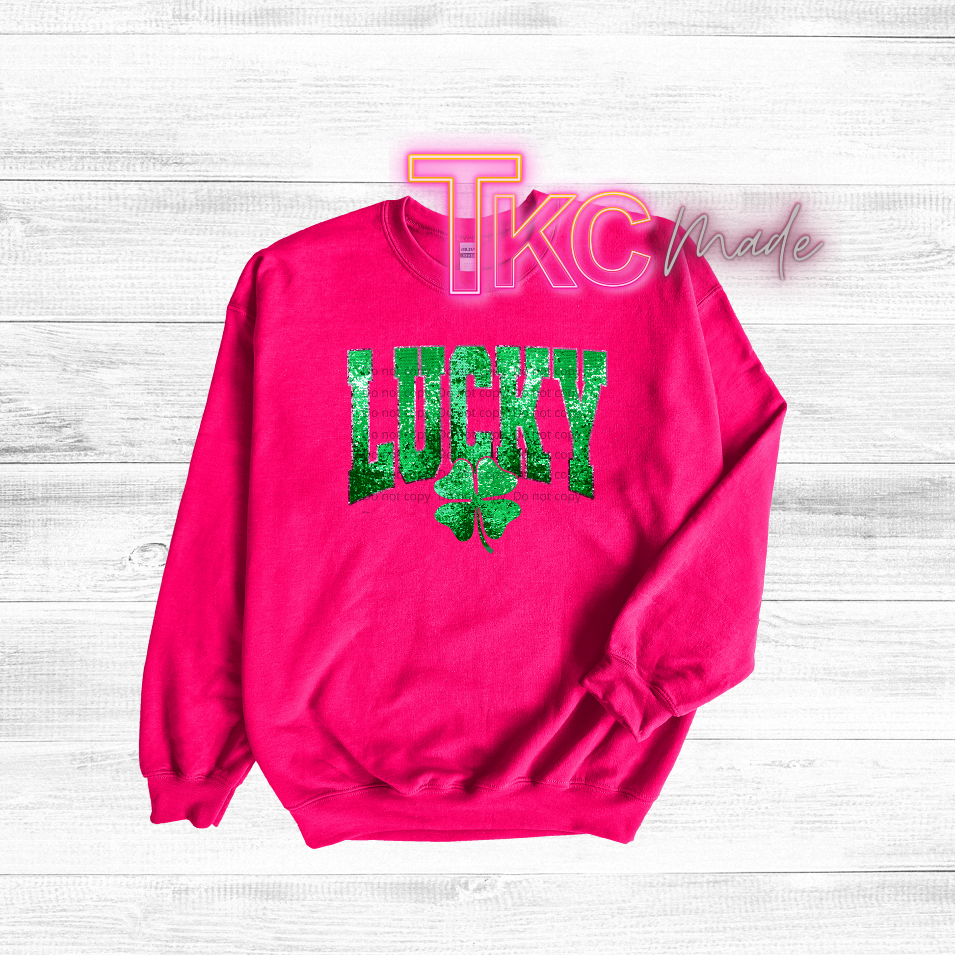 Hot pink sweatshirt with 'Lucky' and shamrock design on a light wooden background
