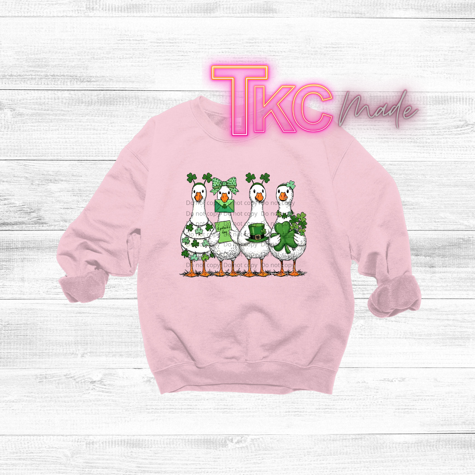 Pink sweatshirt with cartoon geese and 'TKC' branding on a light wooden background