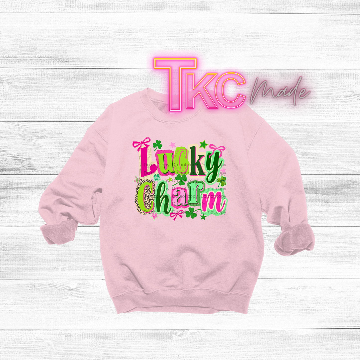 Pink sweatshirt with 'Lucky Charm' text  in different colors and patterns on a white wooden background