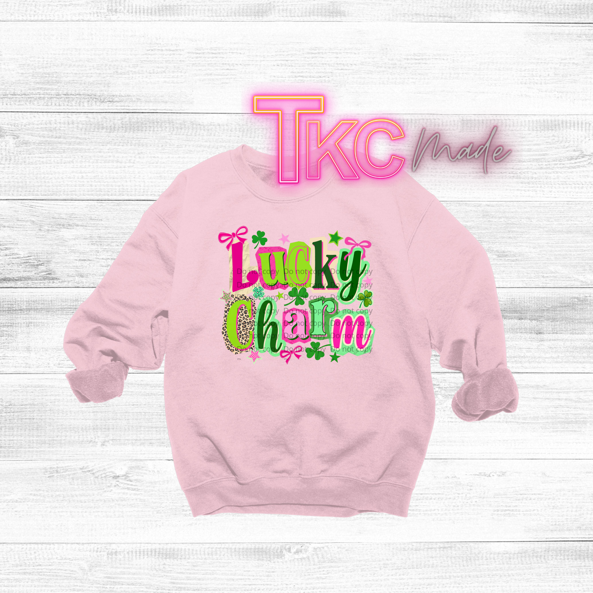 Pink sweatshirt with 'Lucky Charm' text  in different colors and patterns on a white wooden background