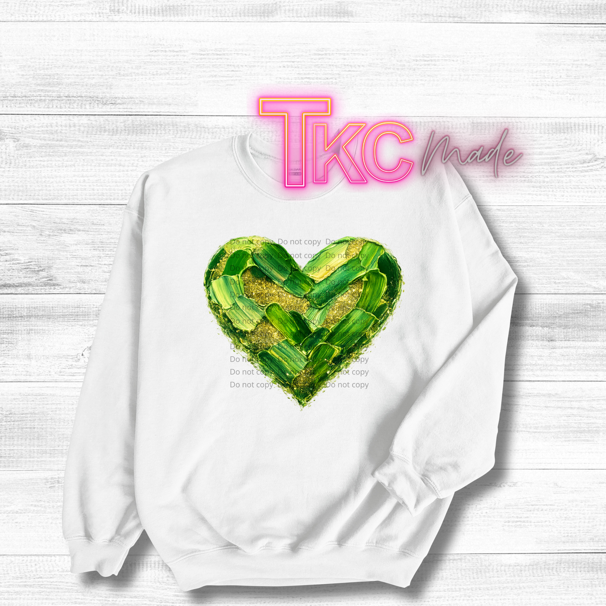 White sweatshirt with a green heart design and 'TKC made' text on a light wood background