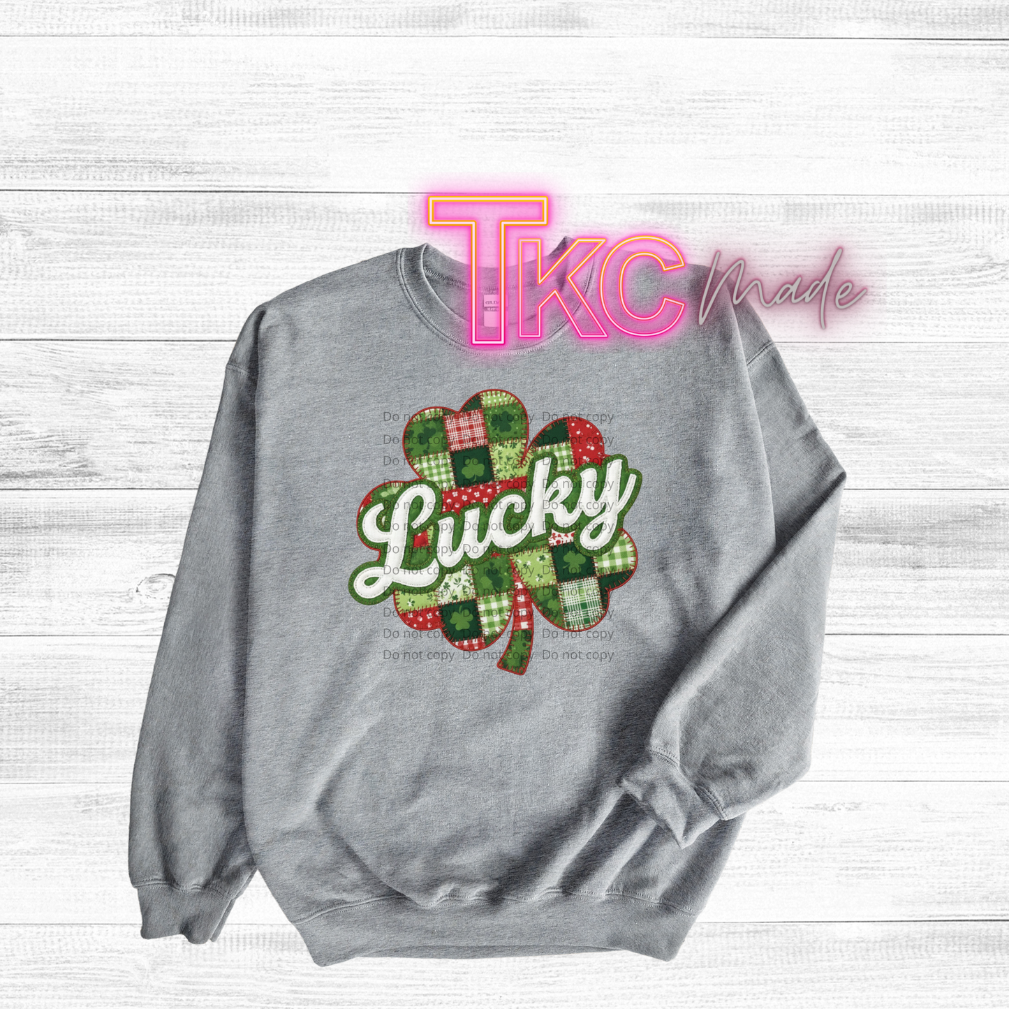 Gray sweatshirt with a plaid shamrock design and 'Lucky' text on a white wooden background, featuring 'TKC made' branding.