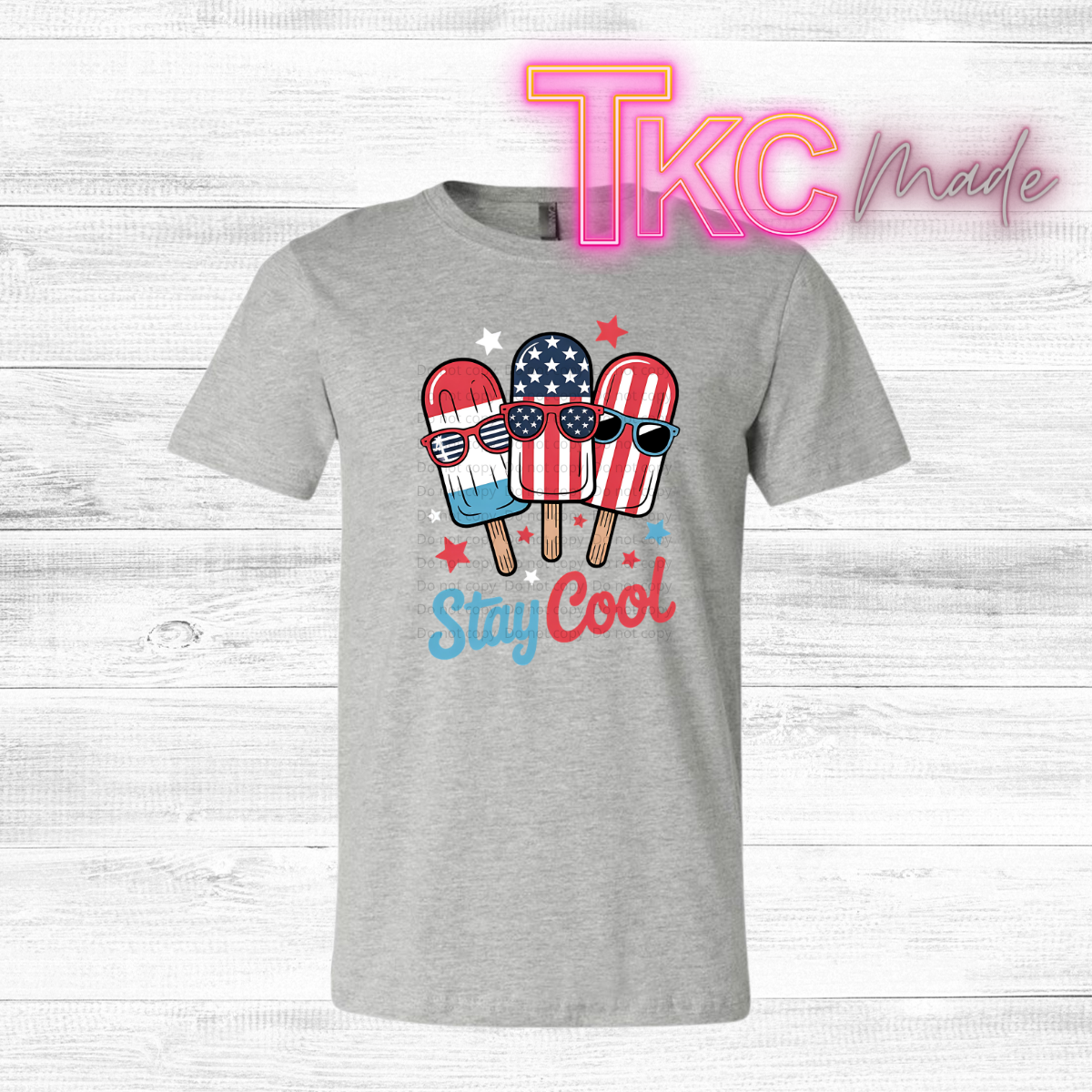 Gray t-shirt with ice cream popsicles wearing American flags and sunglasses, text 'Stay Cool', and 'TKC made' branding on a light wood background.