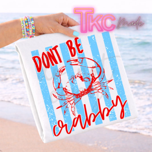 Towel with 'Don't be crabby' text and a crab graphic, held by a person on a beach.