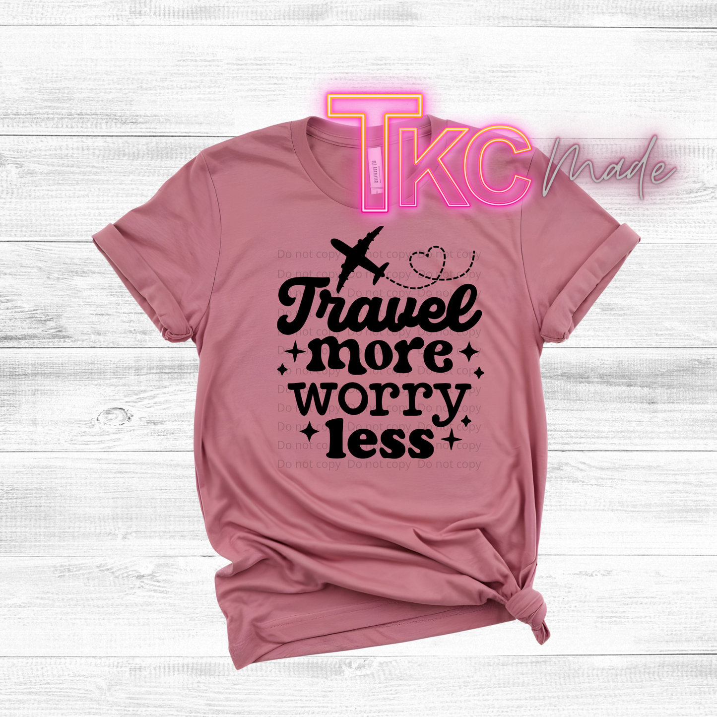 Pink t-shirt with 'Travel more, Worry less' text on a light wooden background