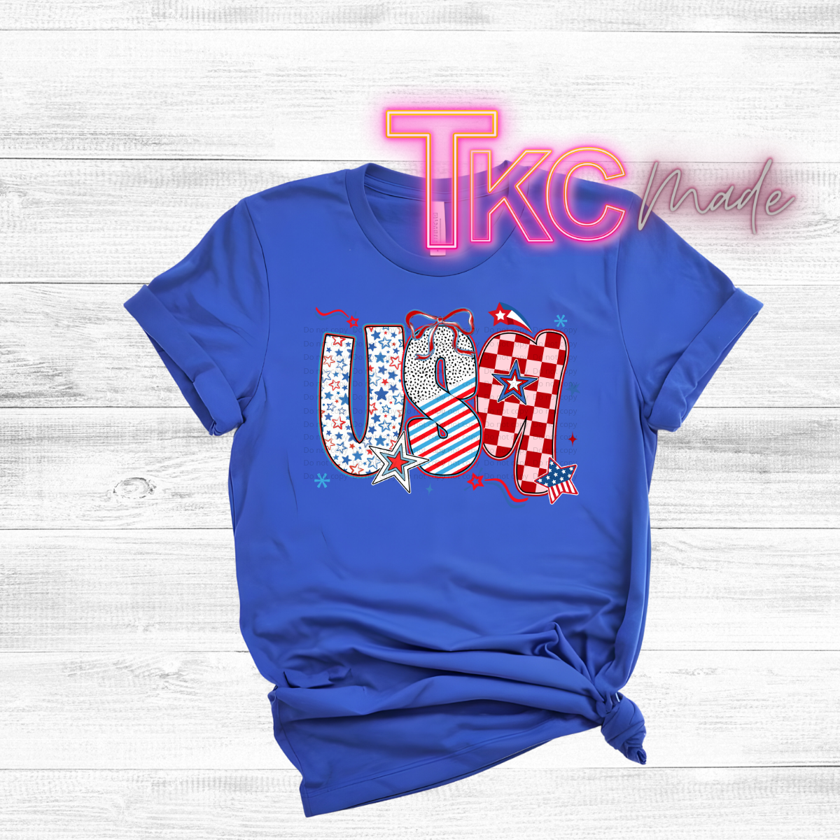 Blue t-shirt with 'USA' design and 'TKC Made' branding on a wooden surface