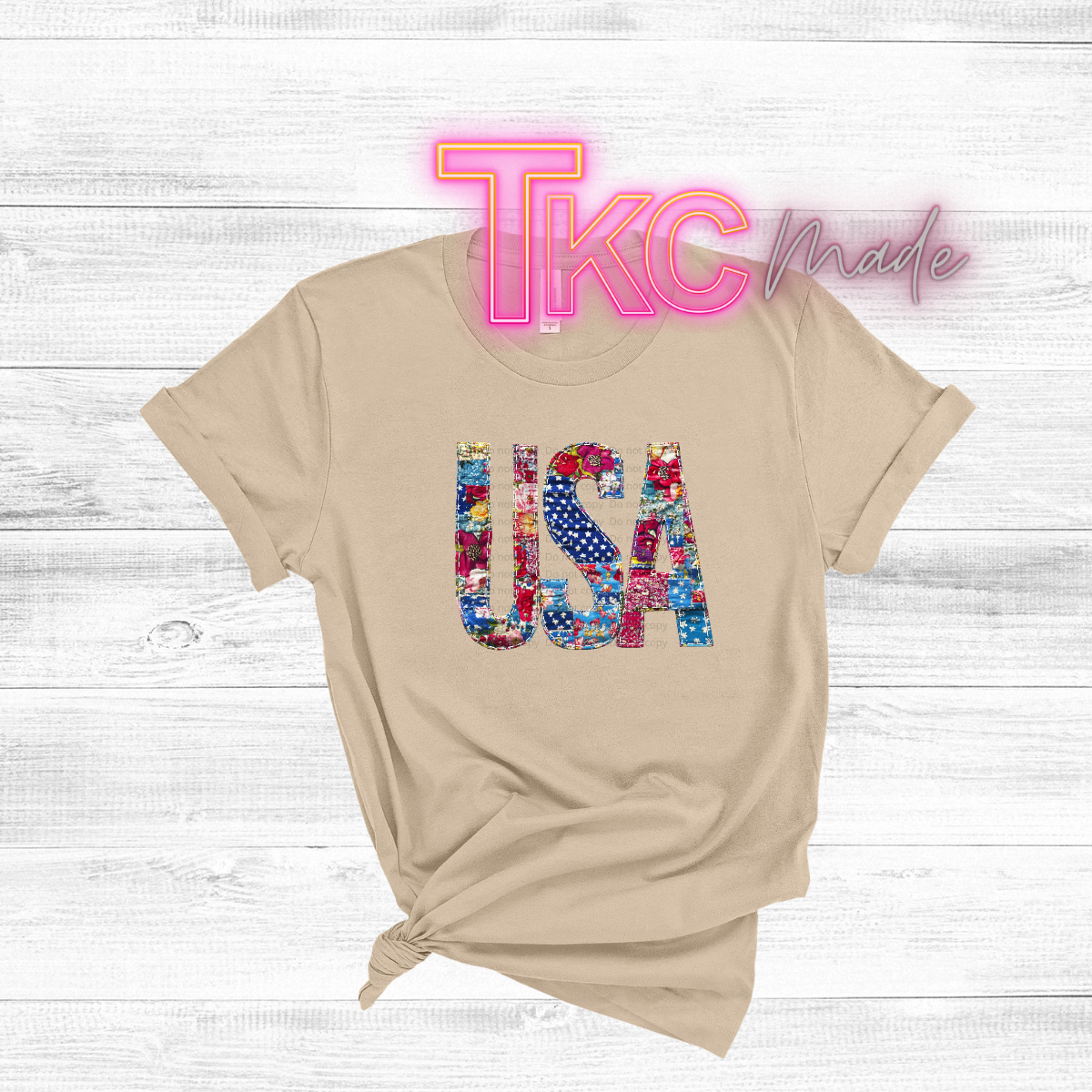 Beige t-shirt with colorful 'USA' design and 'TKC Made' text on a light wooden background