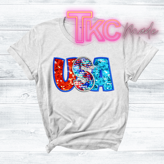 White t-shirt with colorful 'USA' design and 'TKC Made' text on a white background